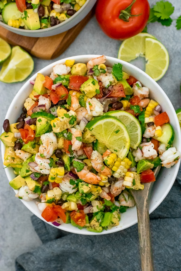 White bowl filled with salad that contains shrimp, avocados, tomatoes, onion, and various vegetables. All tossed with a cilantro lime dressing.