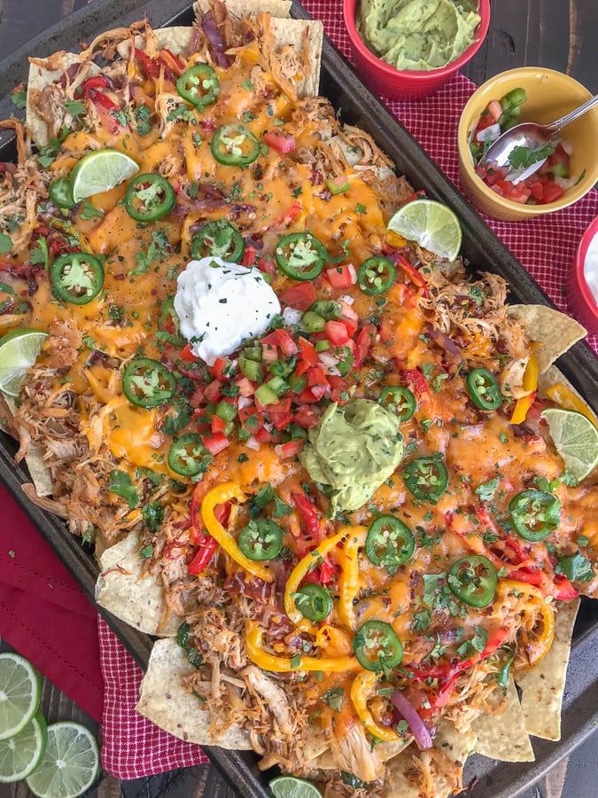 Loaded Chipotle Chicken Carnitas Nachos - more than likely the easiest, most flavor-packed nachos you will ever make! These nachos are loaded with chipotle chicken carnitas, salsa, cheese, sautéed onions and peppers, jalapeños, and topped with some amazing dips! #nachos #carnitas #loadnachos #mexican #tacotuesday #cincodemayo | https://withpeanutbutterontop.com