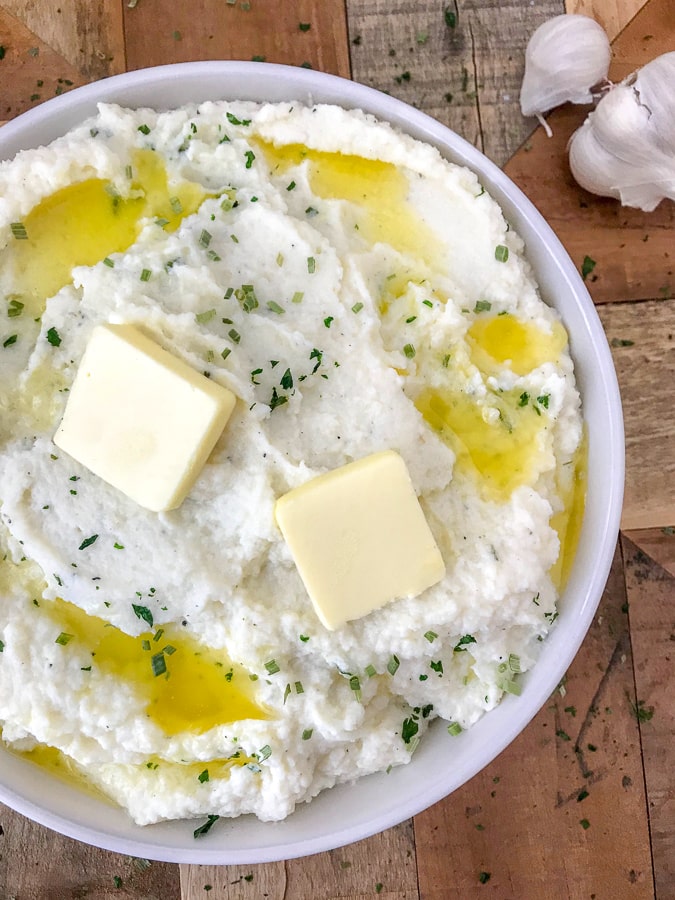 Garlic Parmesan Mashed Cauliflower - an easy, low-carb, healthier version of the traditional buttery, herb-filled mashed potatoes we all know and love! You won't even be able to taste the difference. #lowcarb #mashedcauliflower #cauliflowerpotatoes #healthy #sidedish | https://withpeanutbutterontop.com