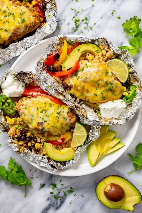 White plate with two grilled foil packets filled with veggies and chicken.